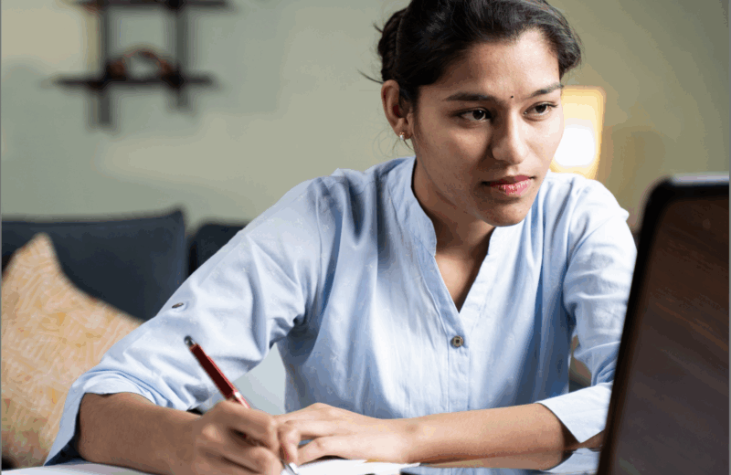Woman taking notes while looking at a computer screen.